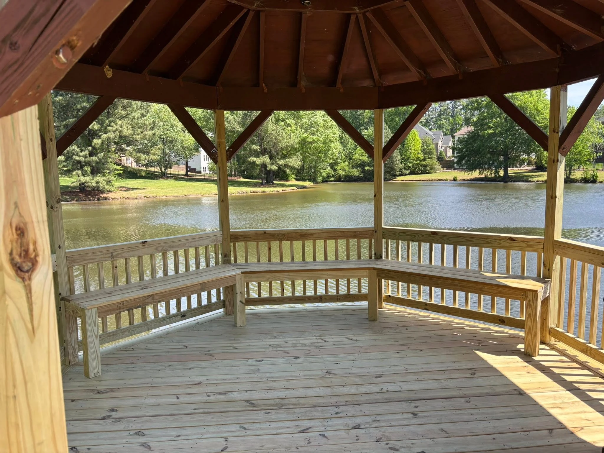 Custom wooden lake gazebo with built-in wraparound benches and stained vaulted ceiling built by Deck By Deck